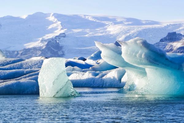 Icebergs float in a glacial lagoon with snow-covered mountains in the background.