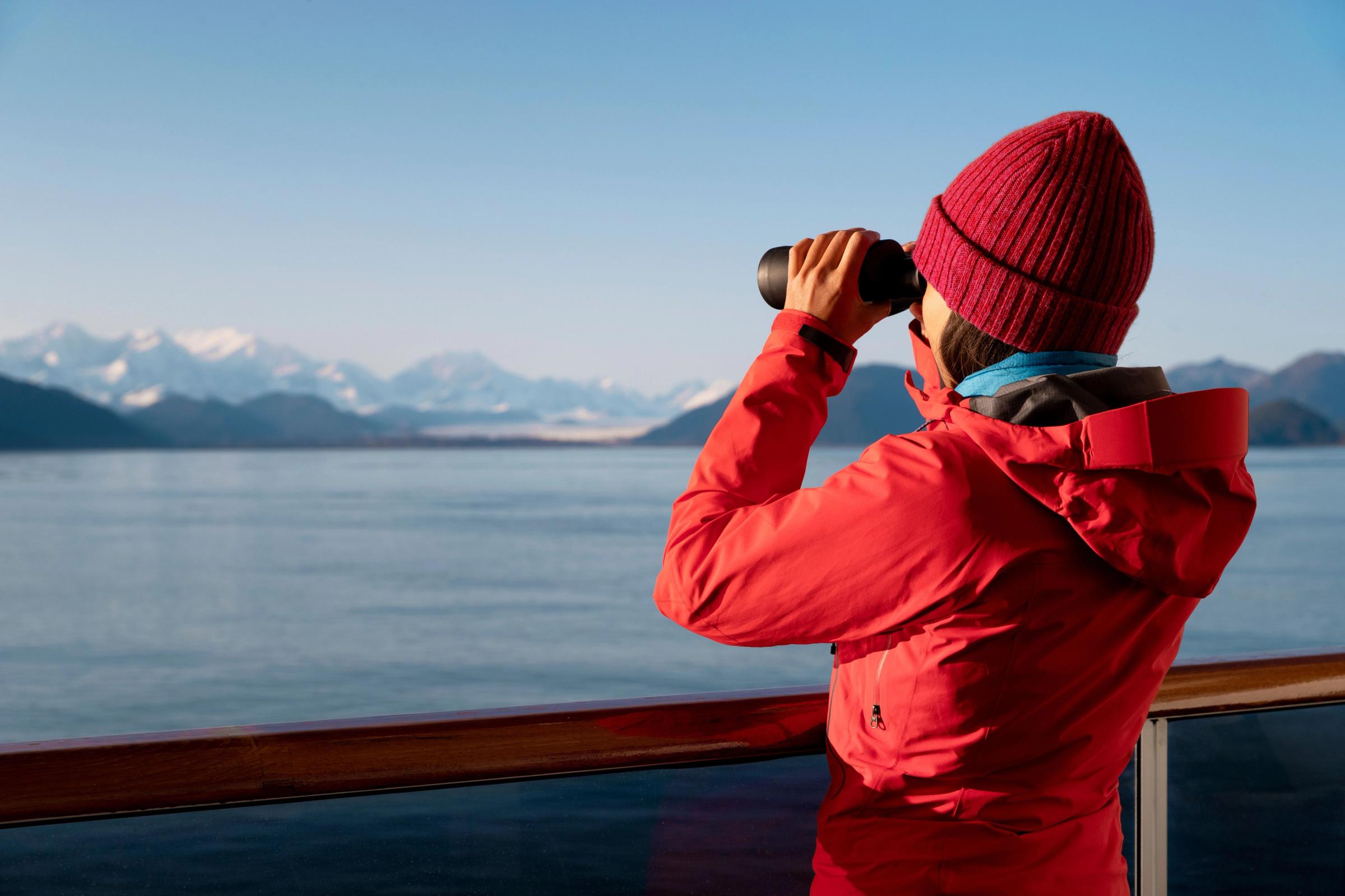 una mujer con una chaqueta roja está mirando a través de unos binoculares en un barco.