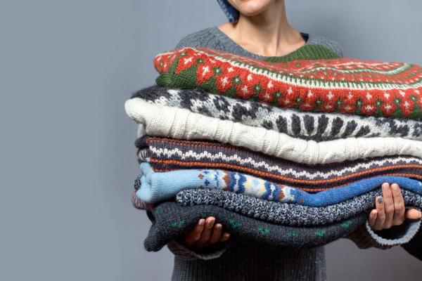 a woman is holding a pile of sweaters in her hands .