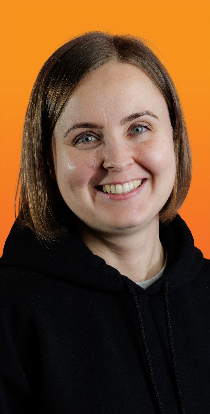 a woman wearing a black hoodie smiles in front of an orange background