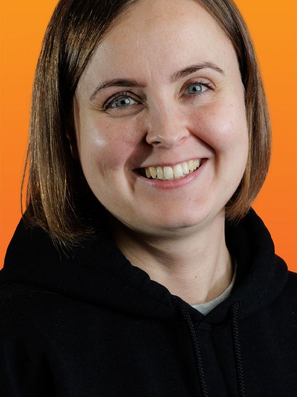 a woman wearing a black hoodie smiles in front of an orange background