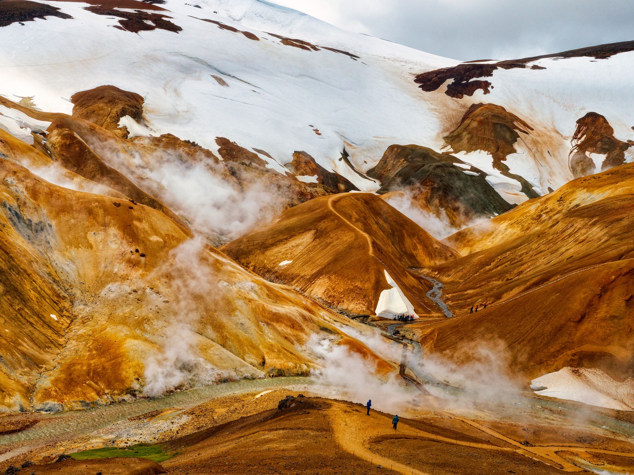 a group of people are walking down a dirt path in the mountains at Hveradlir in Kerlingarfjöll in iceland.