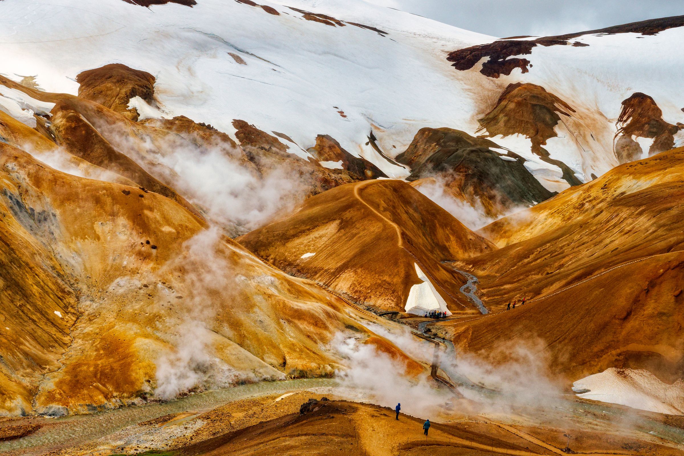 a group of people are walking down a dirt path in the mountains at Hveradlir in Kerlingarfjöll in iceland.