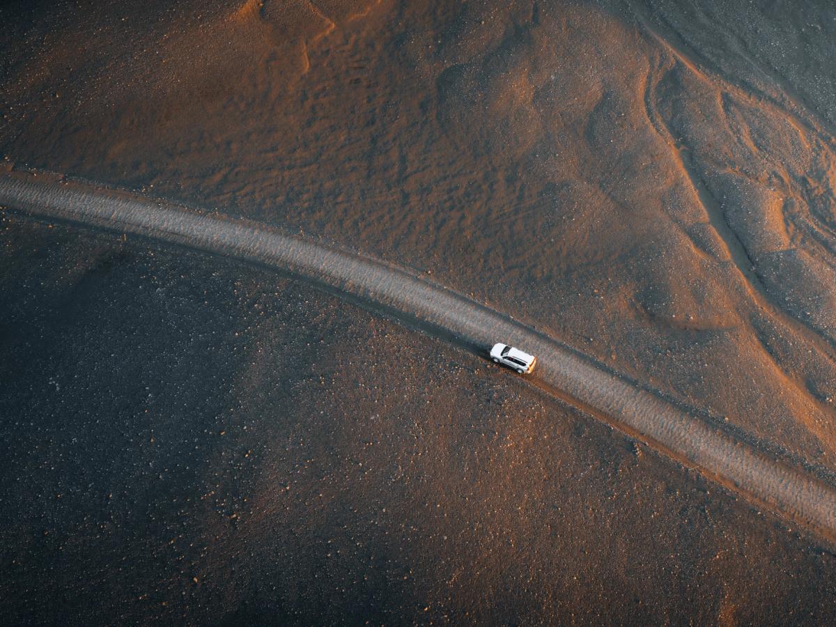 Land Cruiser aus der Vogelperspektive Toyota Land Cruiser aus der Vogelperspektive auf einer schmalen Straße, die durch dunklen Sand führt