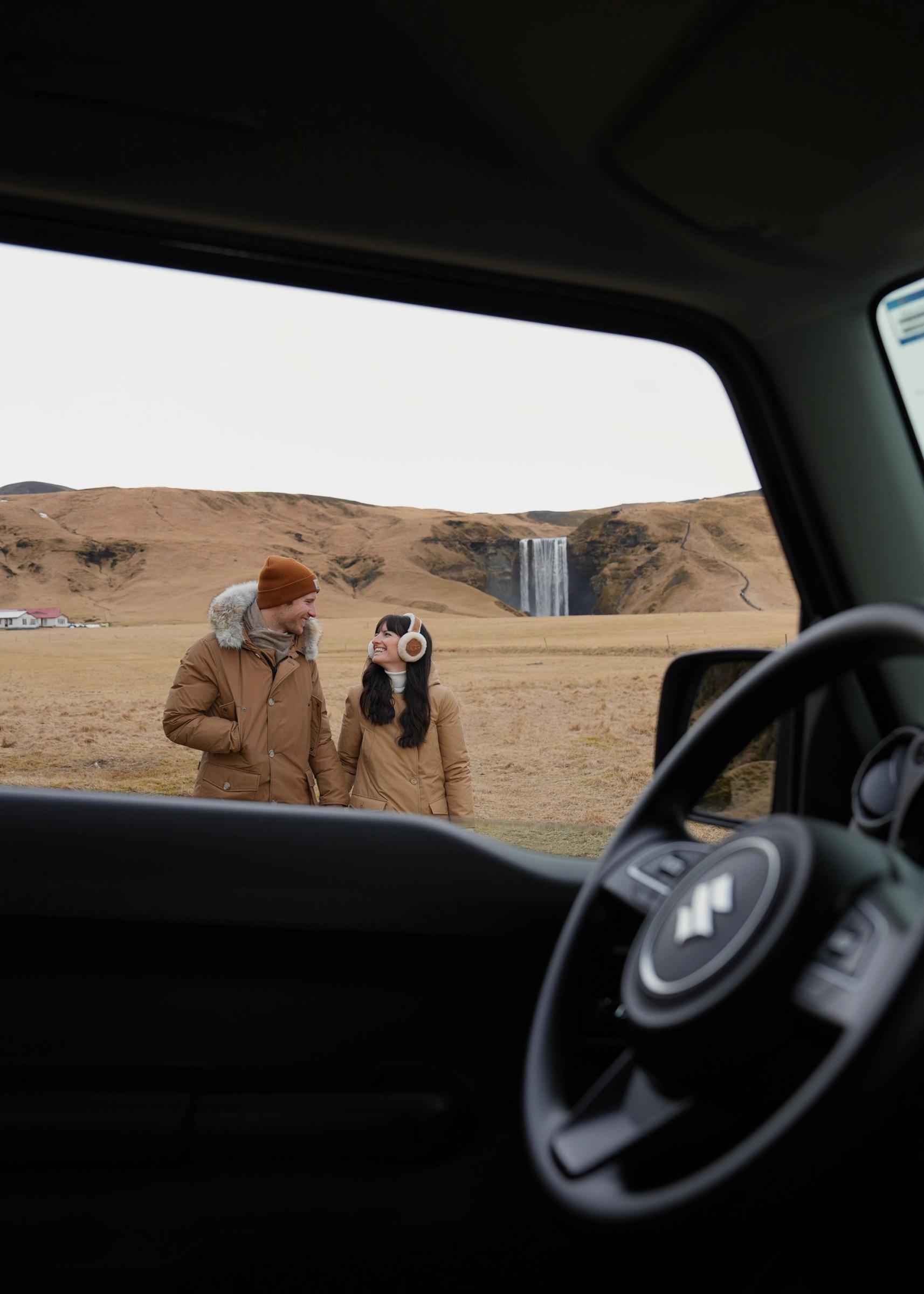Image of a couple through a car window, with Skogafoss in the background