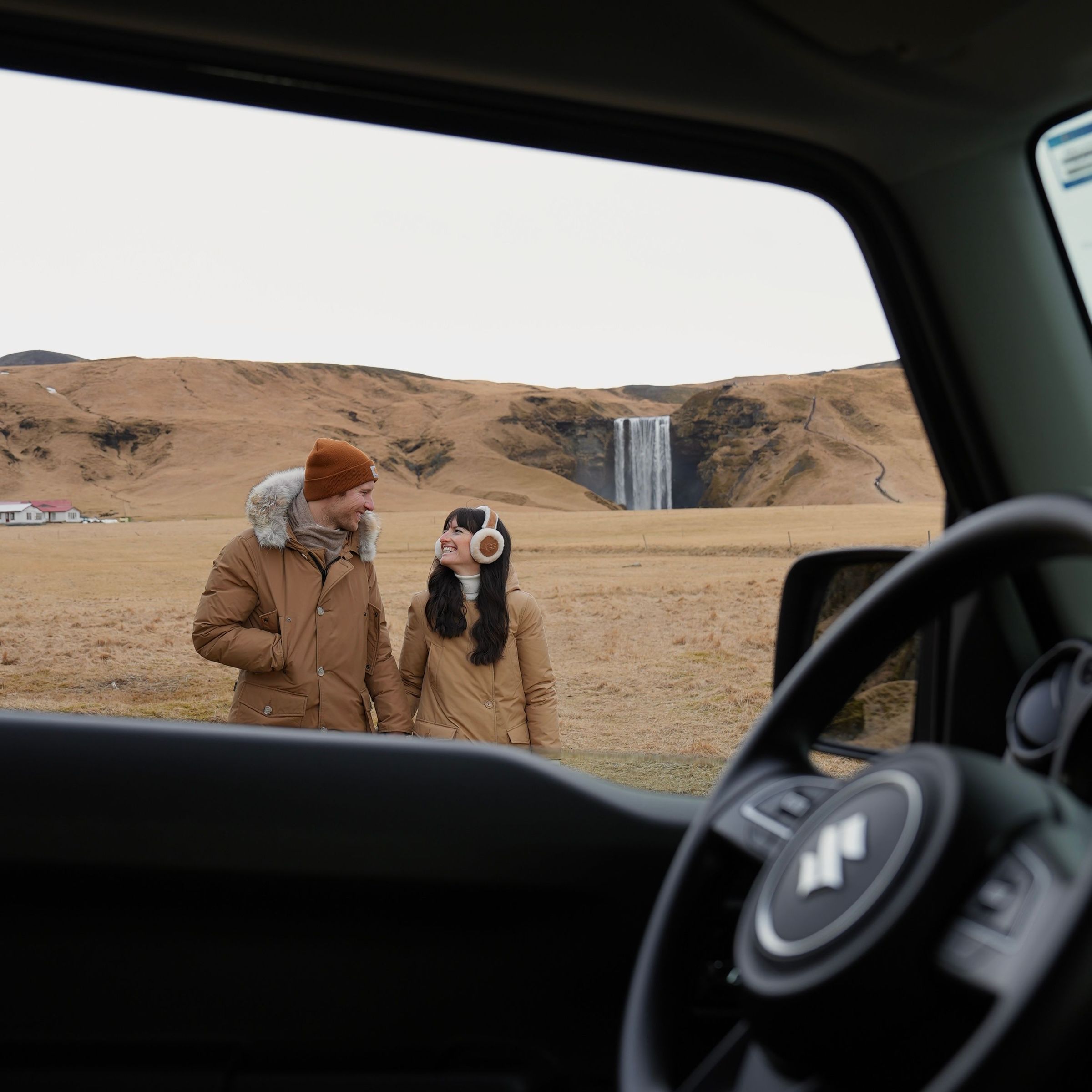 Image of a couple through a car window, with Skogafoss in the background
