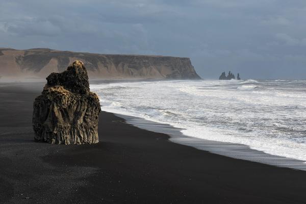 a large rock is sitting on a black sandy beach next to the ocean in iceland.