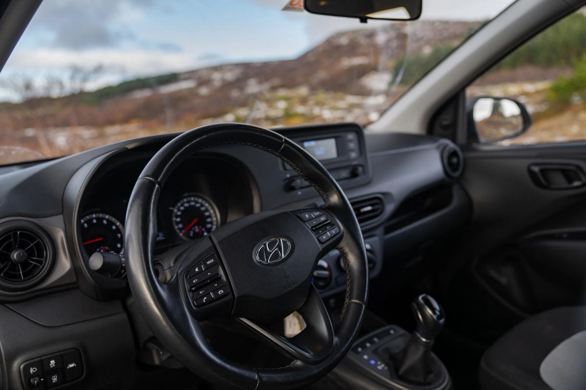 Innenansicht eines Hyundai i10 mit Lenkrad und Armaturenbrett sowie Hügeln im Hintergrund