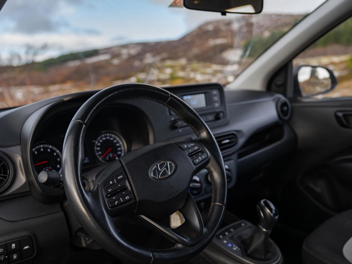 i10-Dashboardansicht Innenansicht eines Hyundai i10 mit Lenkrad und Armaturenbrett sowie Hügeln im Hintergrund