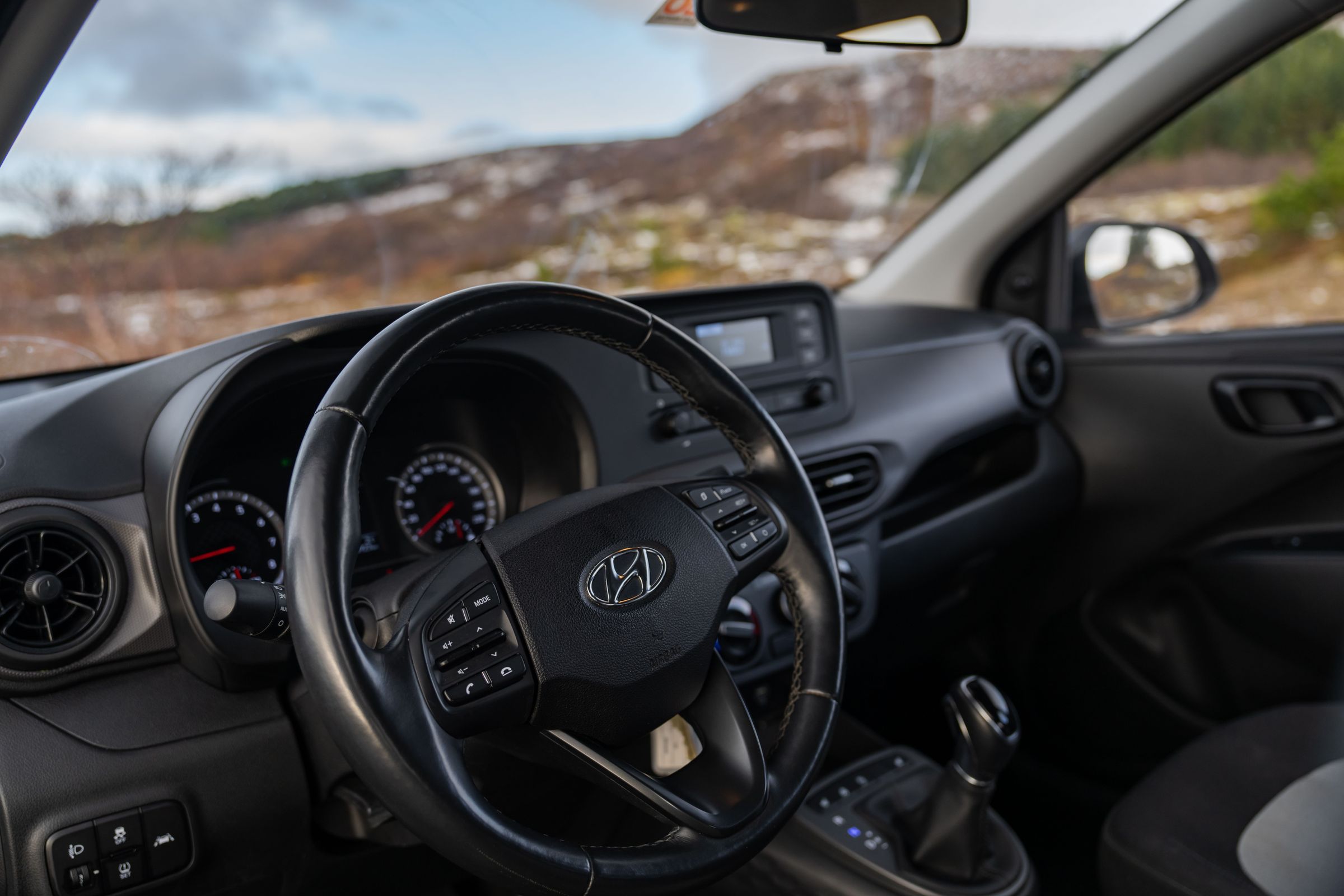 i10-Dashboardansicht Innenansicht eines Hyundai i10 mit Lenkrad und Armaturenbrett sowie Hügeln im Hintergrund