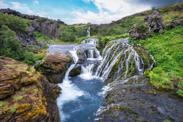 Waterfalls cascading into a pond with rocks and greenery around