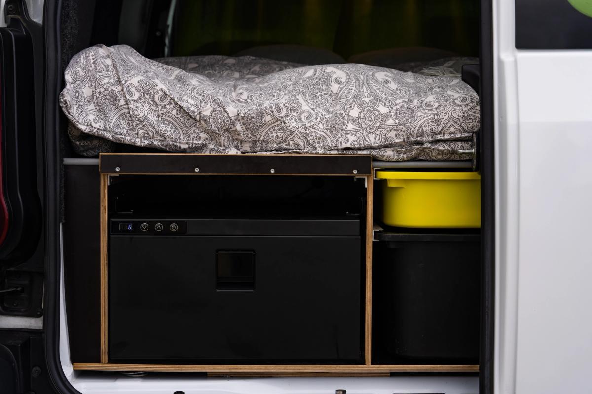 Cajón frigorífico cerrado con botones de control, junto a un recipiente amarillo y un compartimento de almacenamiento debajo de la cama