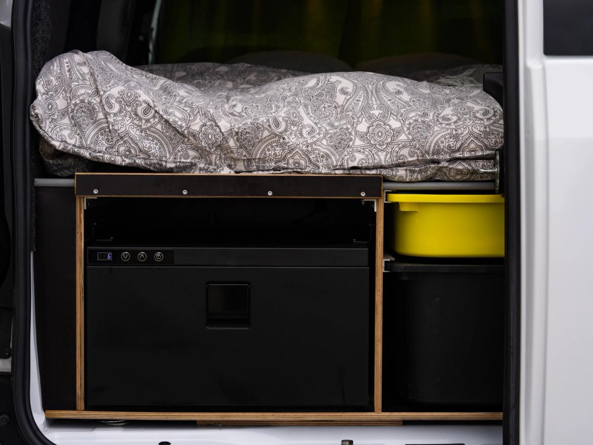 Cajón del frigorífico cerrado Cajón frigorífico cerrado con botones de control, junto a un recipiente amarillo y un compartimento de almacenamiento debajo de la cama