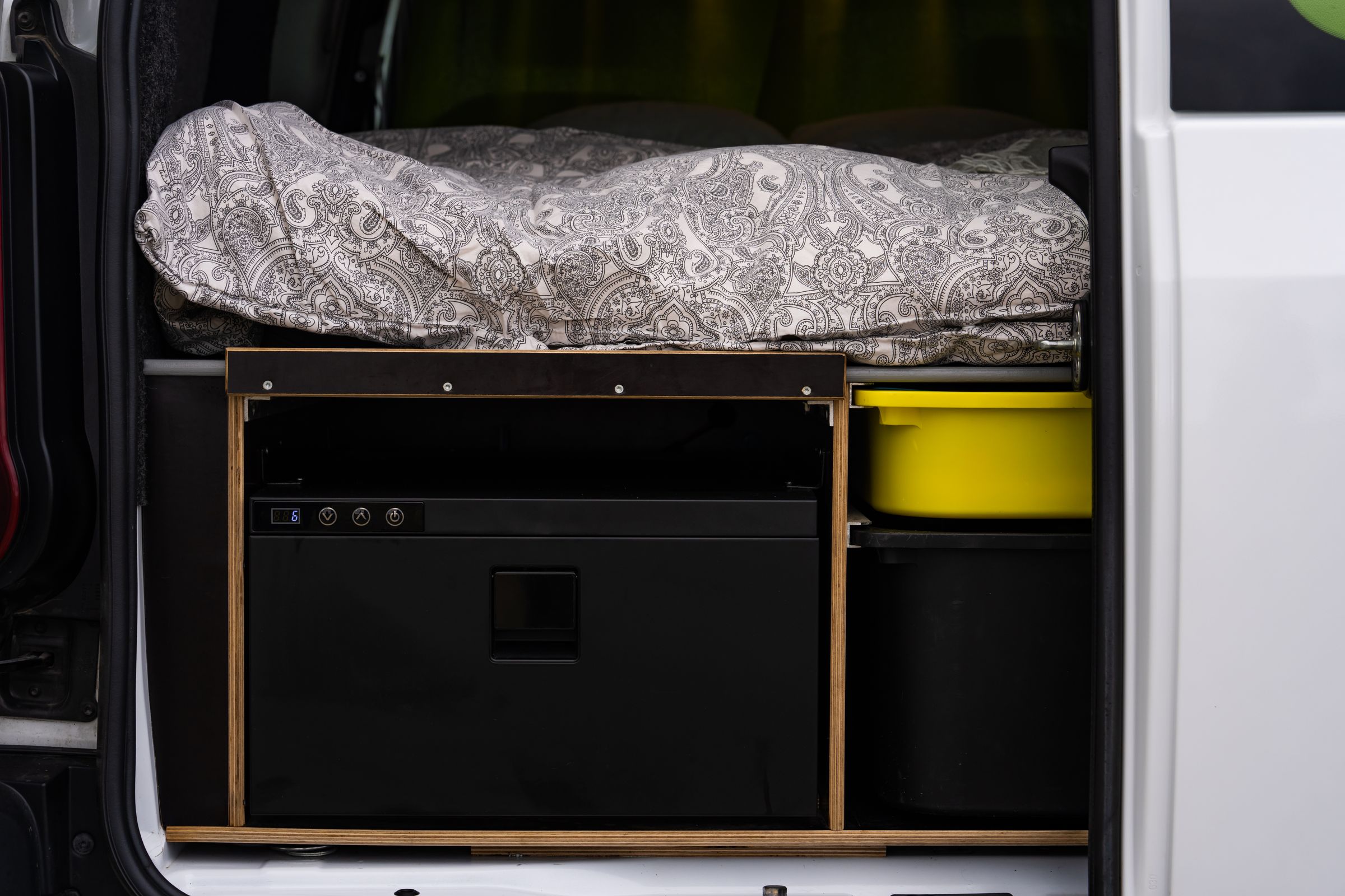 Cajón del frigorífico cerrado Cajón frigorífico cerrado con botones de control, junto a un recipiente amarillo y un compartimento de almacenamiento debajo de la cama