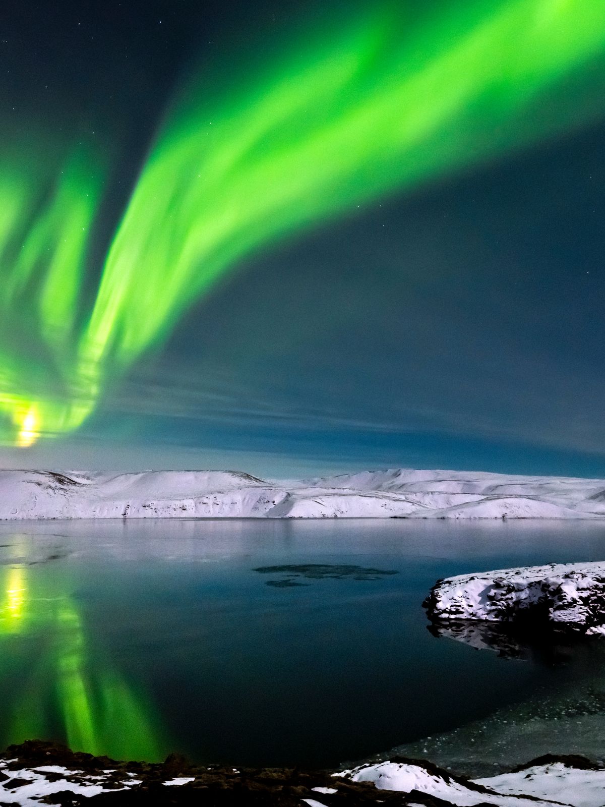 the aurora borealis is reflected in the water of a lake .