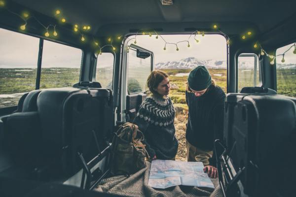 Dos personas miran un mapa en la parte trasera de un vehículo decorado con luces de cuerda, con vistas a un paisaje montañoso.