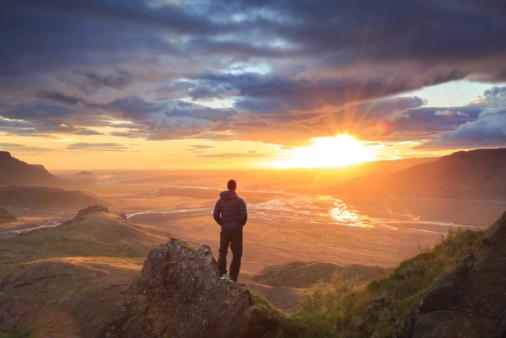a man is standing on top of a mountain looking at the sunset .