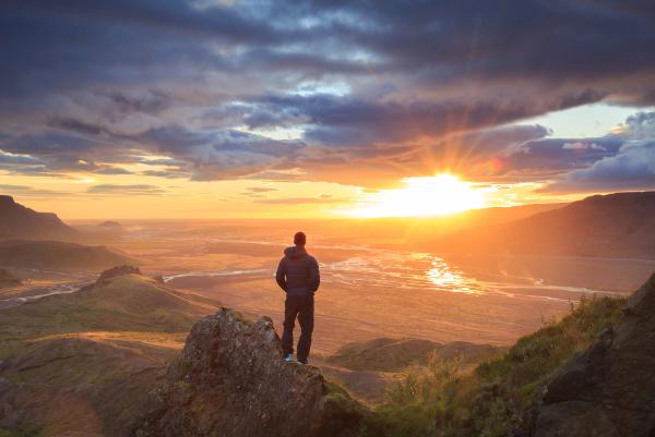 a man is standing on top of a mountain looking at the sunset .