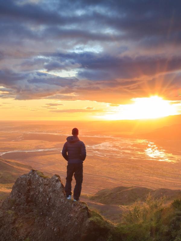 Iceland in April a man is standing on top of a mountain looking at the sunset .
