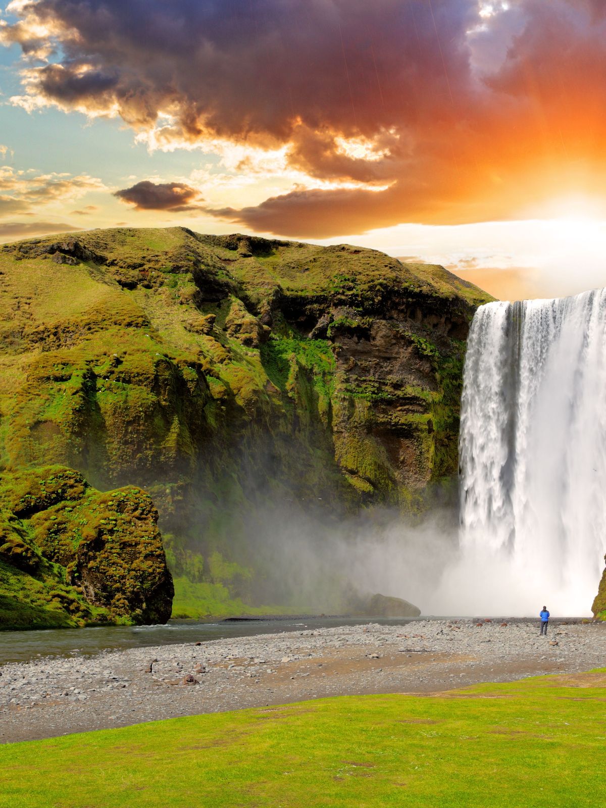 una cascada en medio de un campo verde exuberante con una puesta de sol de fondo .