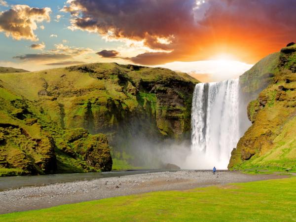a waterfall in the middle of a lush green field with a sunset in the background .