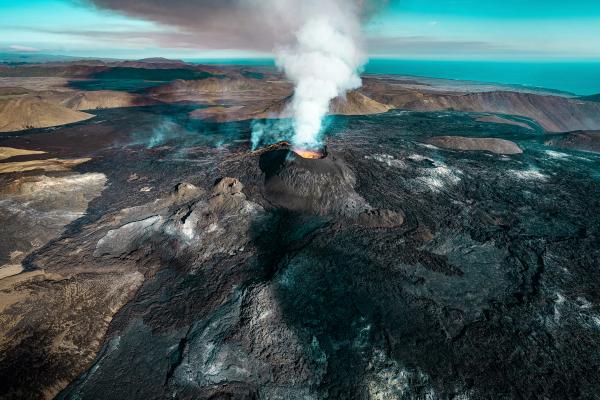 an aerial view of volcano Fagradalsfjall erupting with smoke coming out of it.