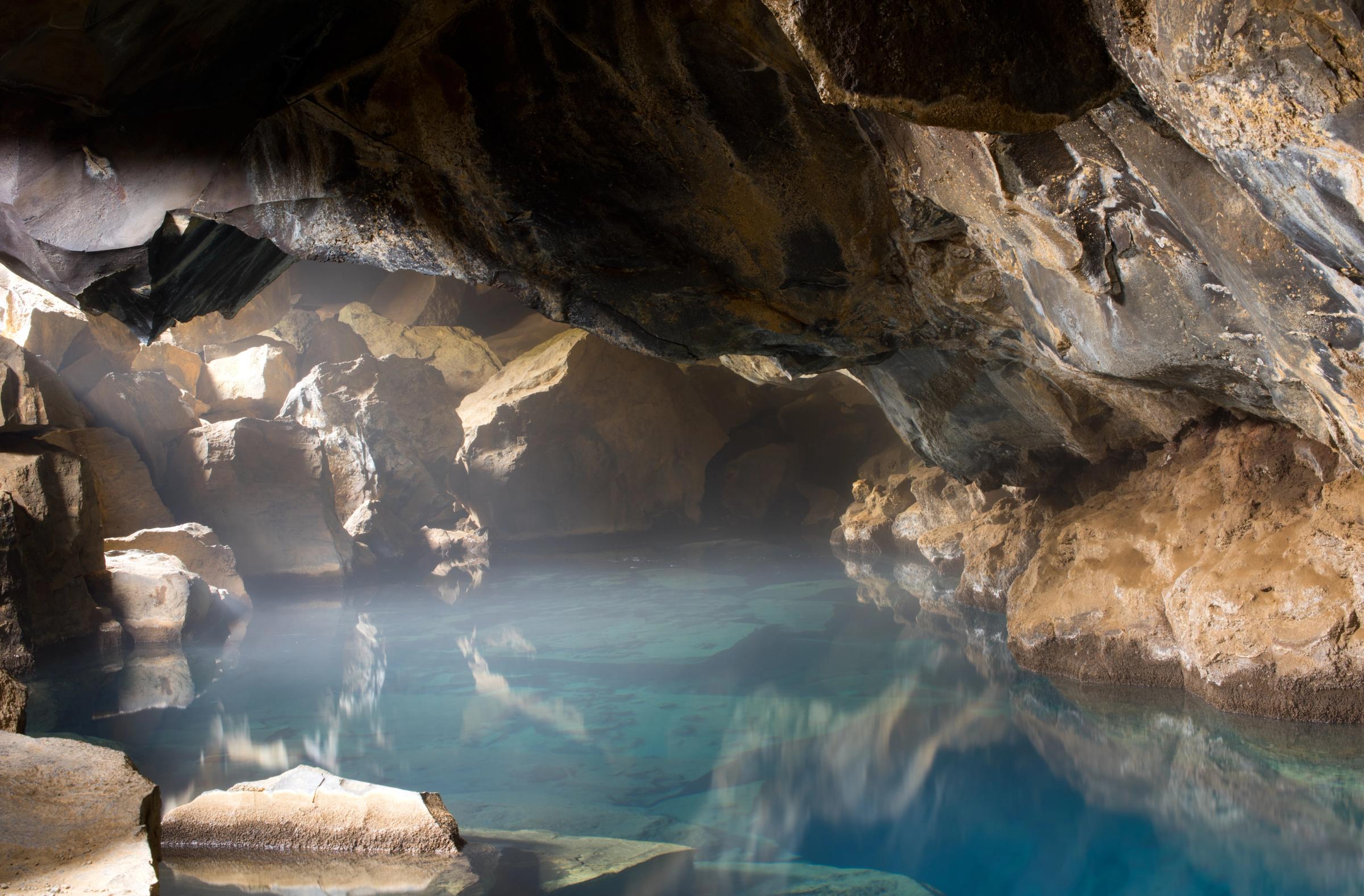 Steaming blue water inside a rocky cave, lit by a beam of light.