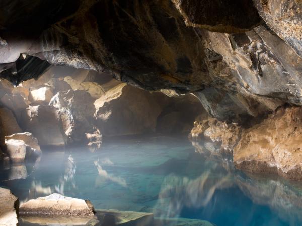 Steaming blue water inside a rocky cave, lit by a beam of light.