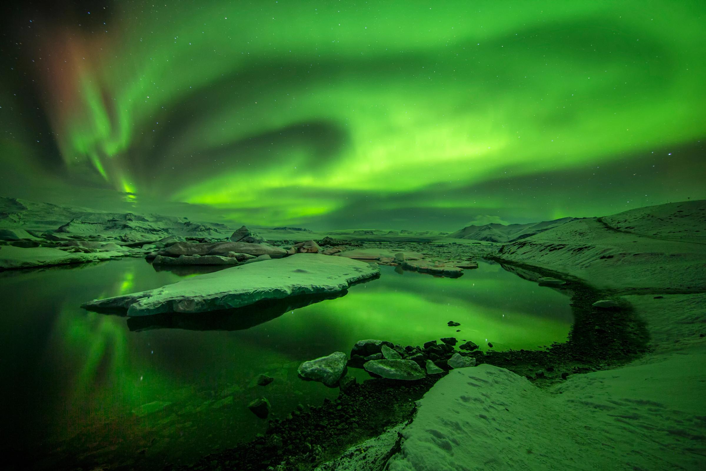 Aurora boreal verde reflejada en un lago glaciar con témpanos de hielo.