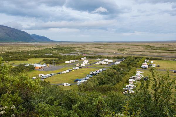 una fila de autocaravanas estacionadas en un campo con montañas al fondo.