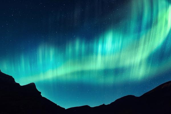 the aurora borealis is dancing in the night sky over the mountains .