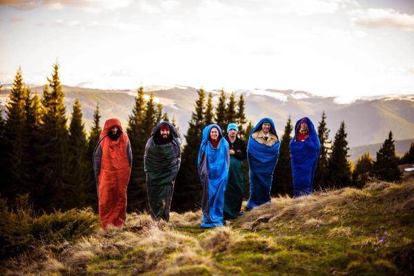 a group of people wrapped in sleeping bags are standing on top of a hill .