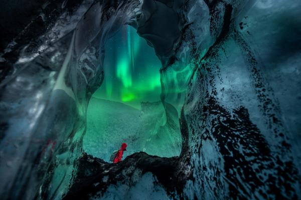 a person is standing in an ice cave under the aurora borealis .