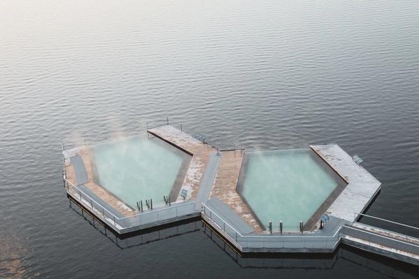 Two hexagonal steaming pools connected by modern walkways, floating on dark water.