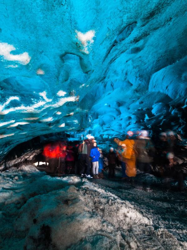 Blurred tourists in a vibrant blue ice cave.