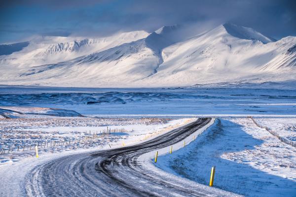 a snowy road with mountains in the background in iceland.