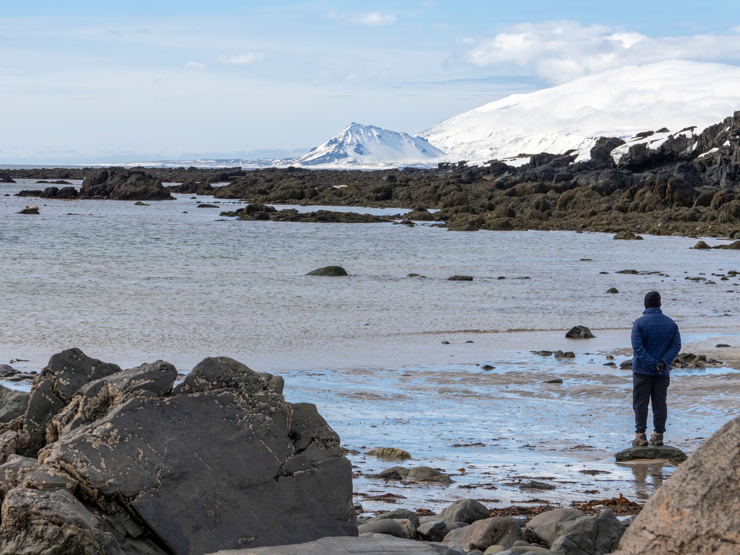 a man is standing on a rocky beach looking at the ocean .