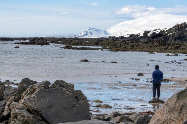 a man is standing on a rocky beach looking at the ocean .