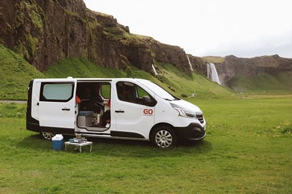 a white van is parked in a grassy field in front of a waterfall in iceland.