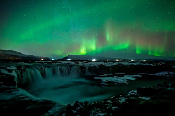 the aurora borealis is shining over a waterfall at night .