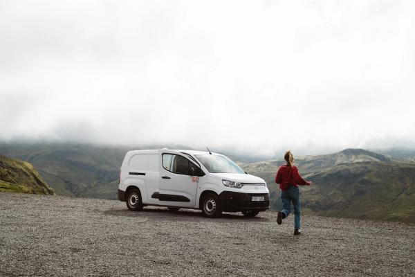 A white van parked on a gravel lot, with a person running nearby, overlooks misty green mountains.