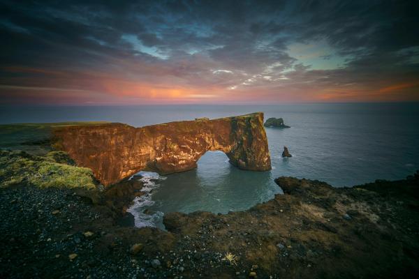 un grand rocher en forme d'arche dans la mer au coucher du soleil