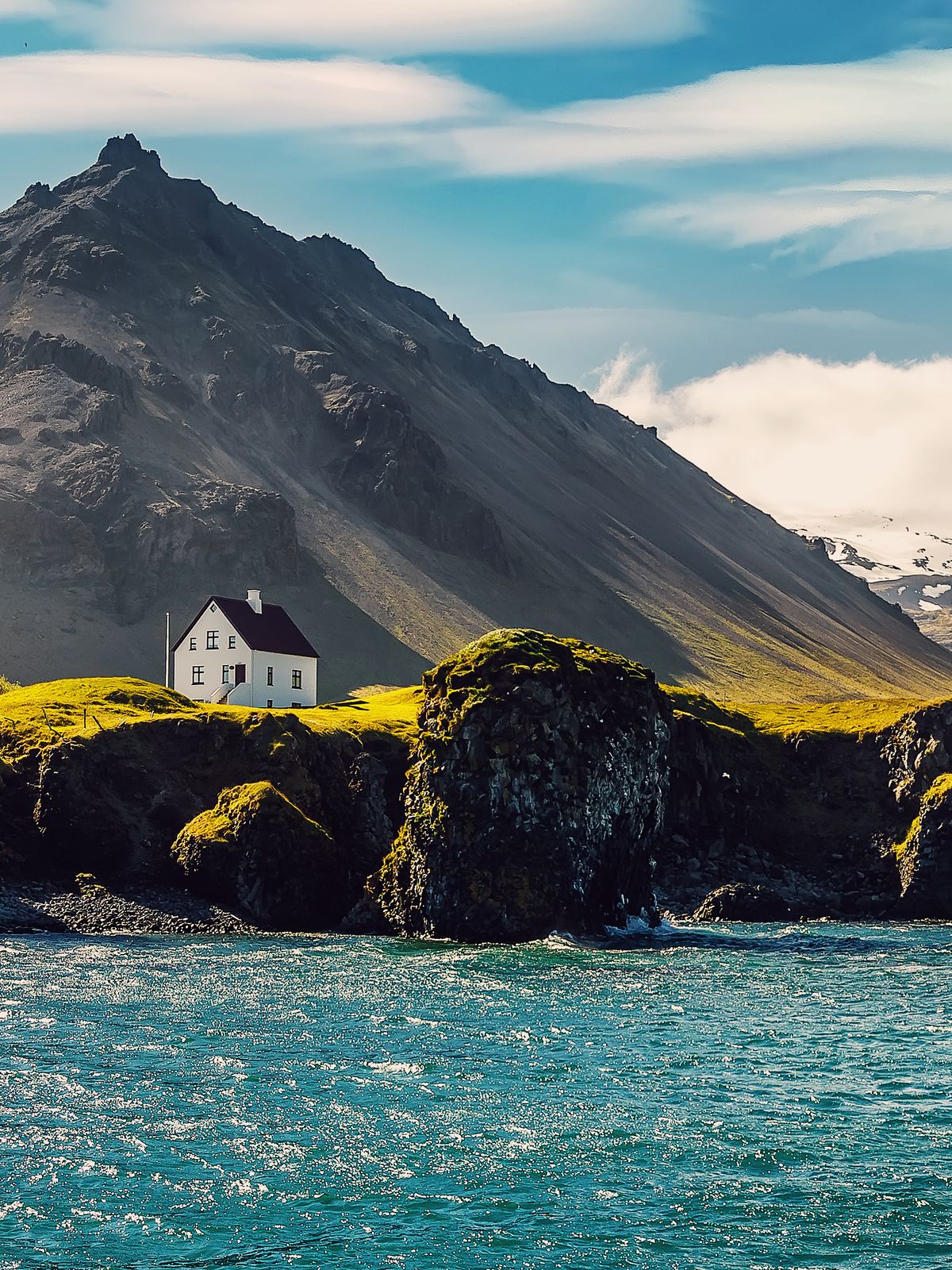 a small white house is sitting on top of a rocky hill next to the ocean .