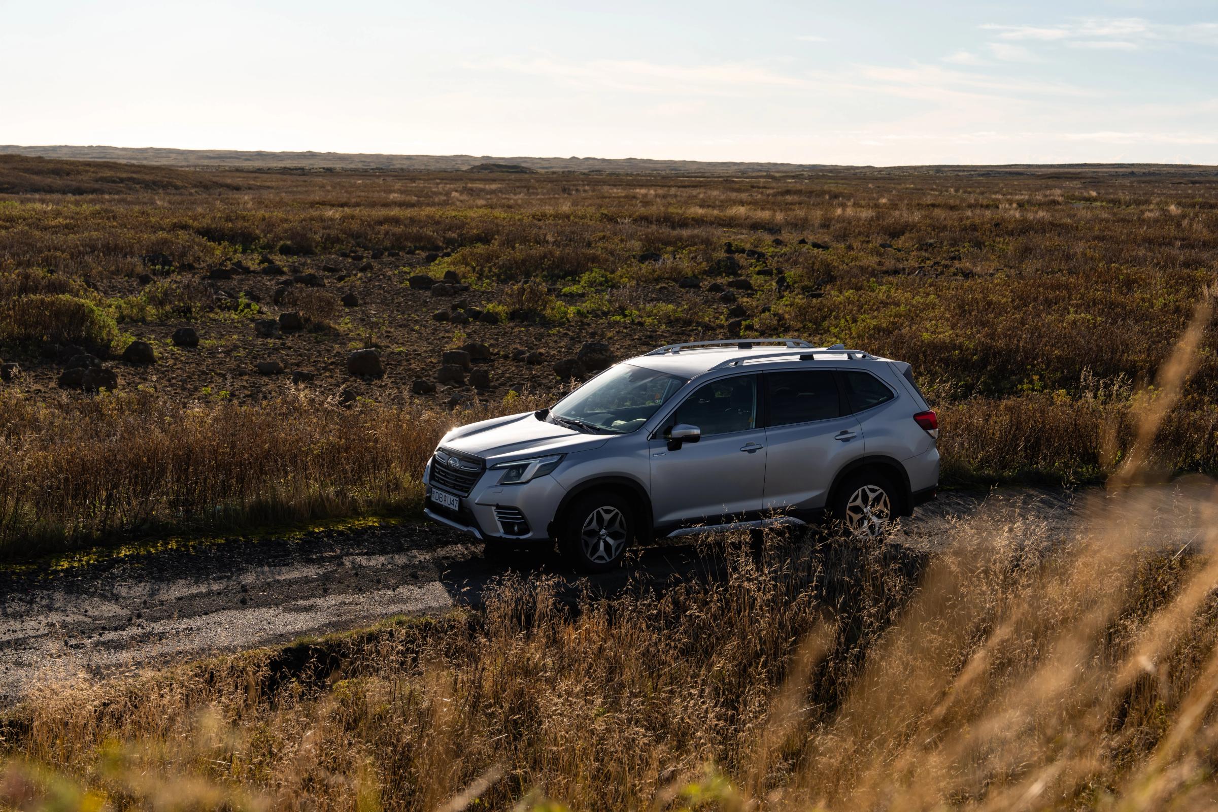 Silver Subaru Forester side view on a gravel track through an open lava field landscape