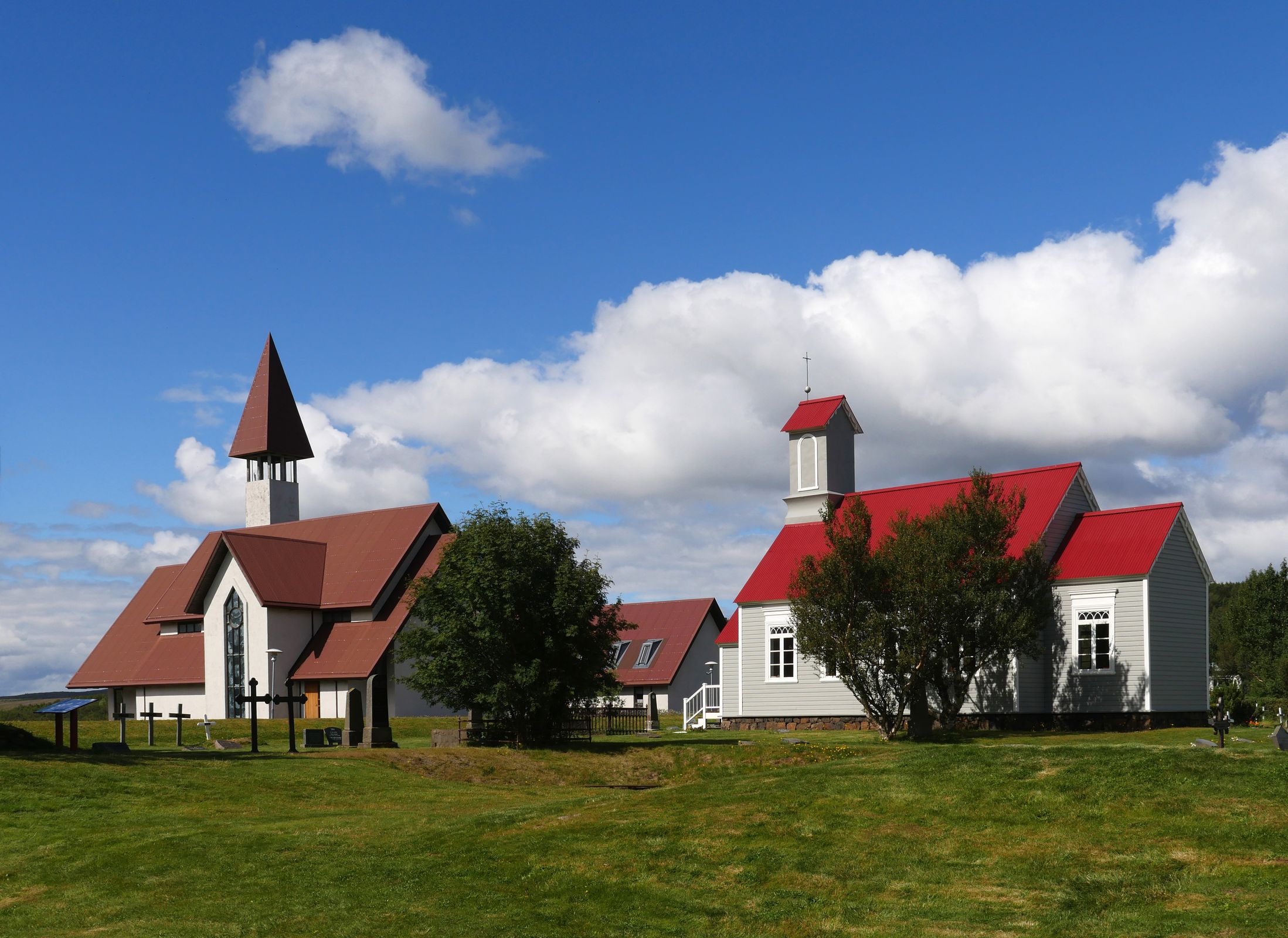 two churches with red roofs are sitting next to each other in a grassy field at Reykholt in iceland.