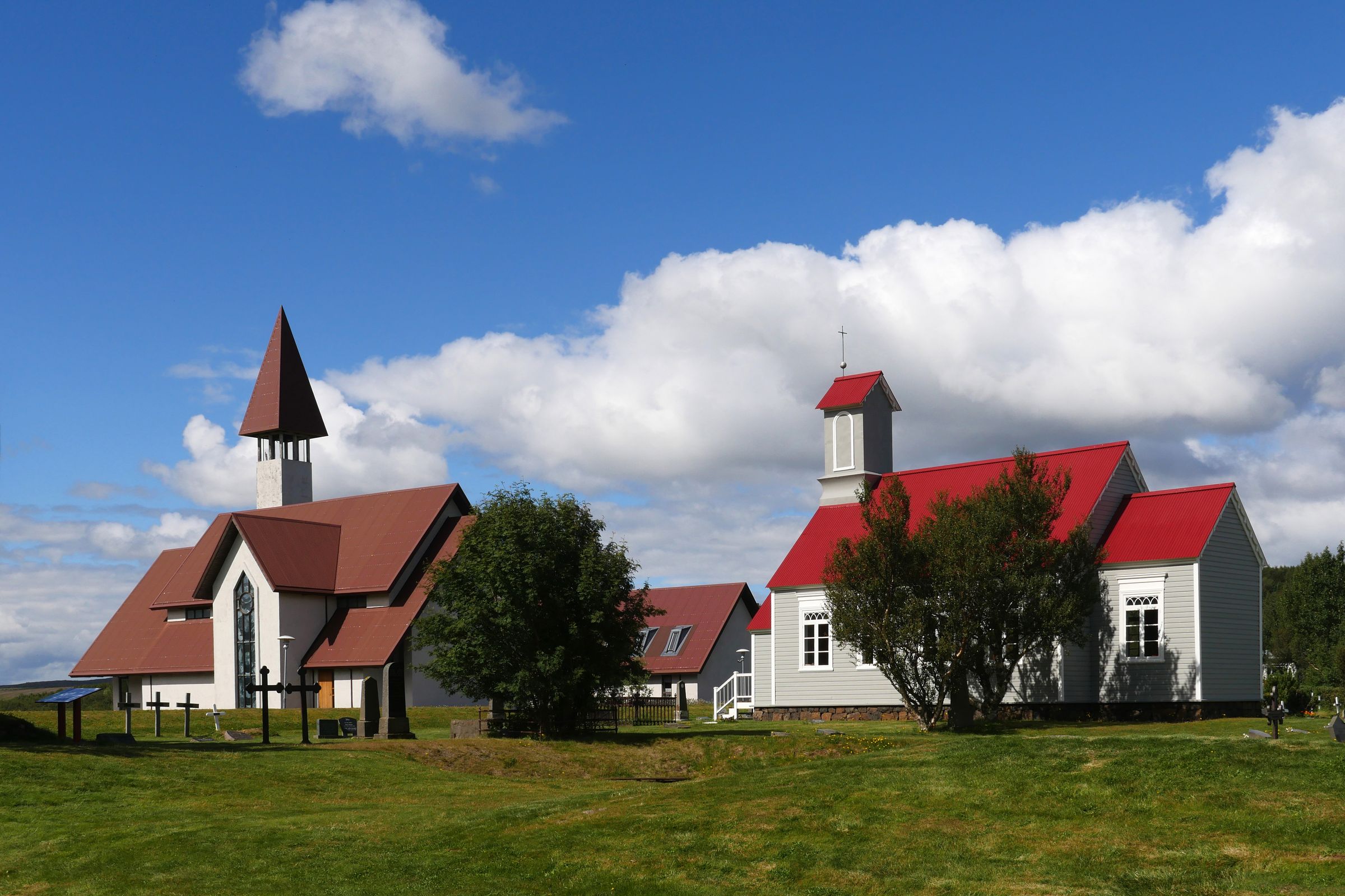 two churches with red roofs are sitting next to each other in a grassy field at Reykholt in iceland.
