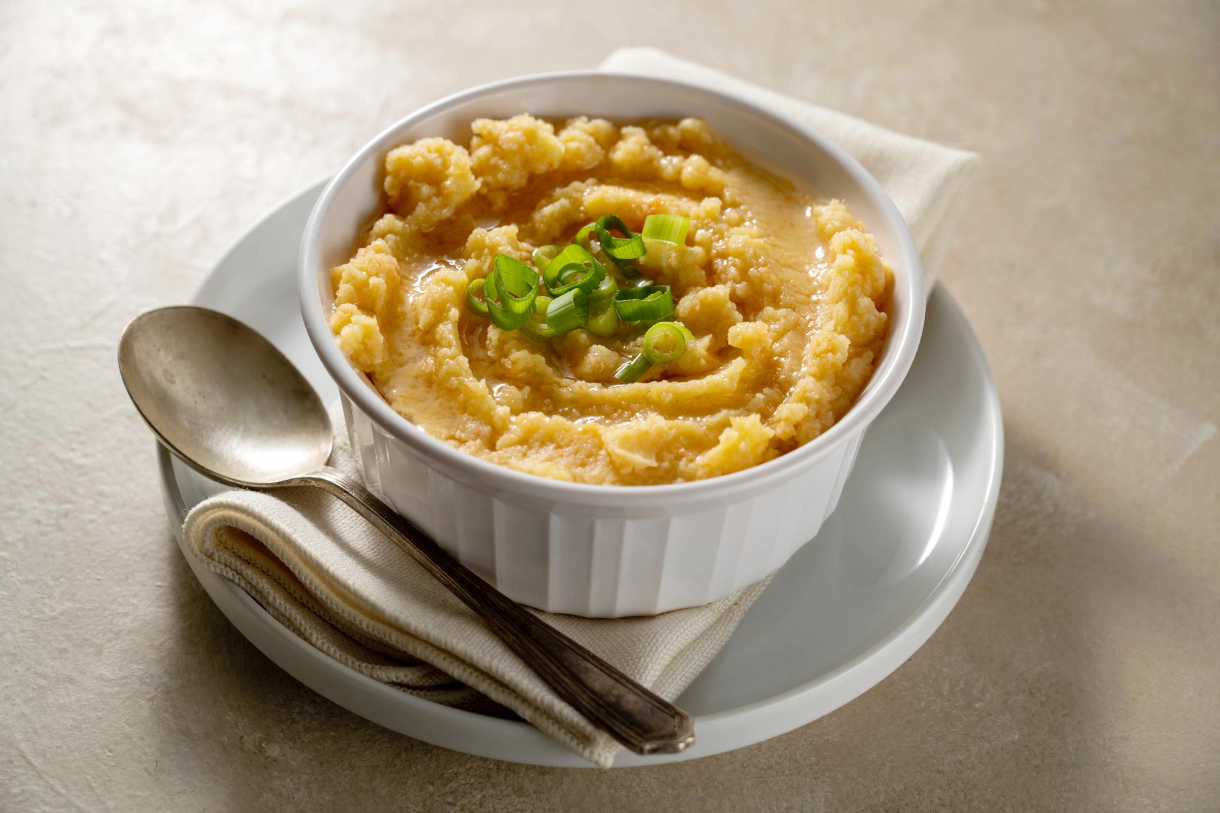A bowl of yellow grits topped with chopped green onions, served with a spoon.