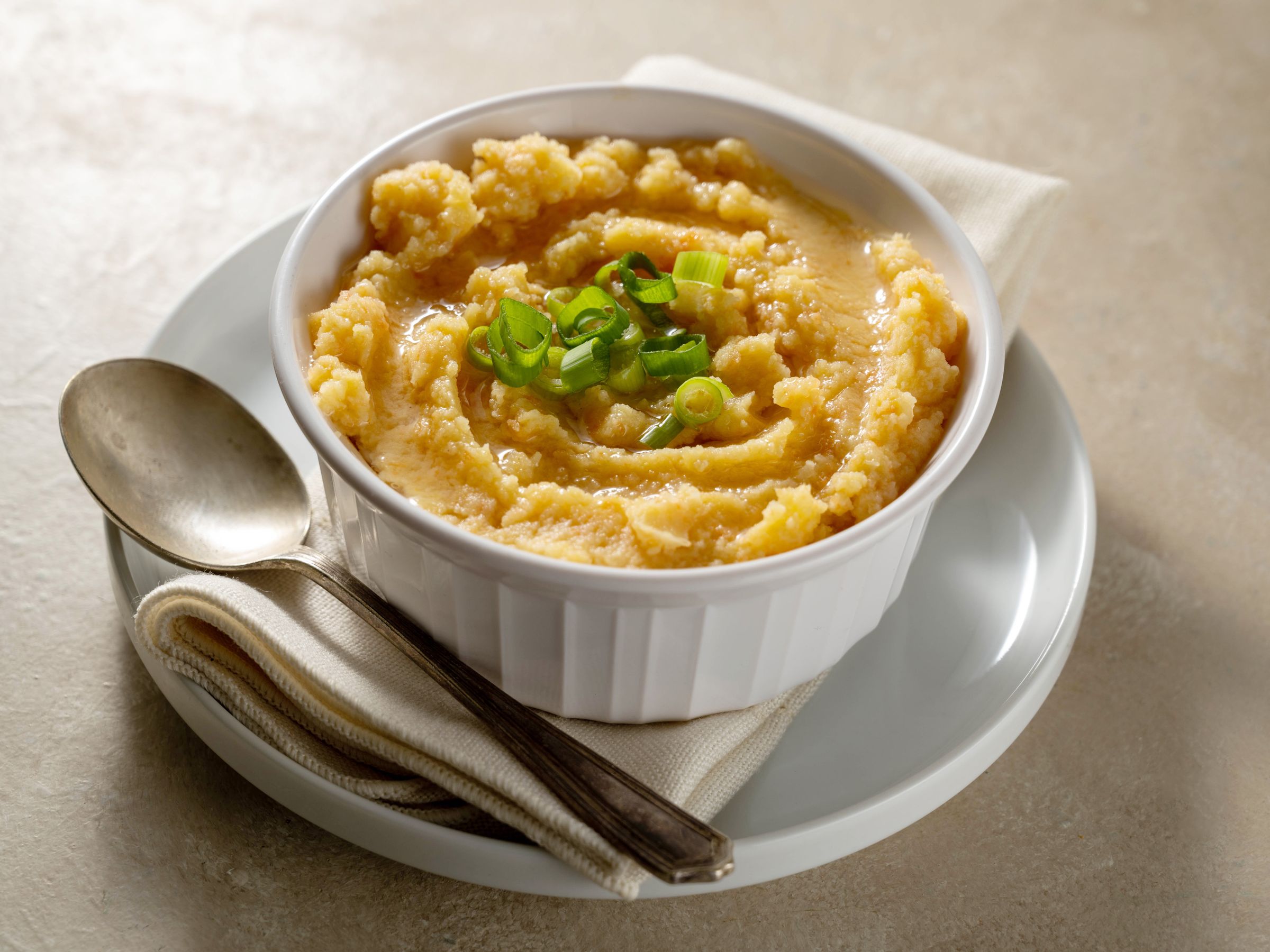 A bowl of yellow grits topped with chopped green onions, served with a spoon.