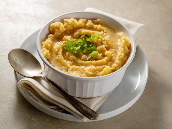 Un tazón de sémola amarilla coronada con cebollas verdes picadas, servido con una cuchara.