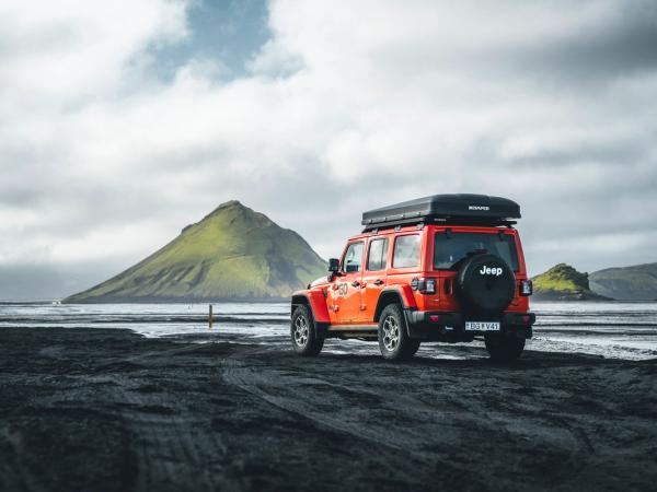 a red jeep is parked on a dirt road in front of a mountain .
